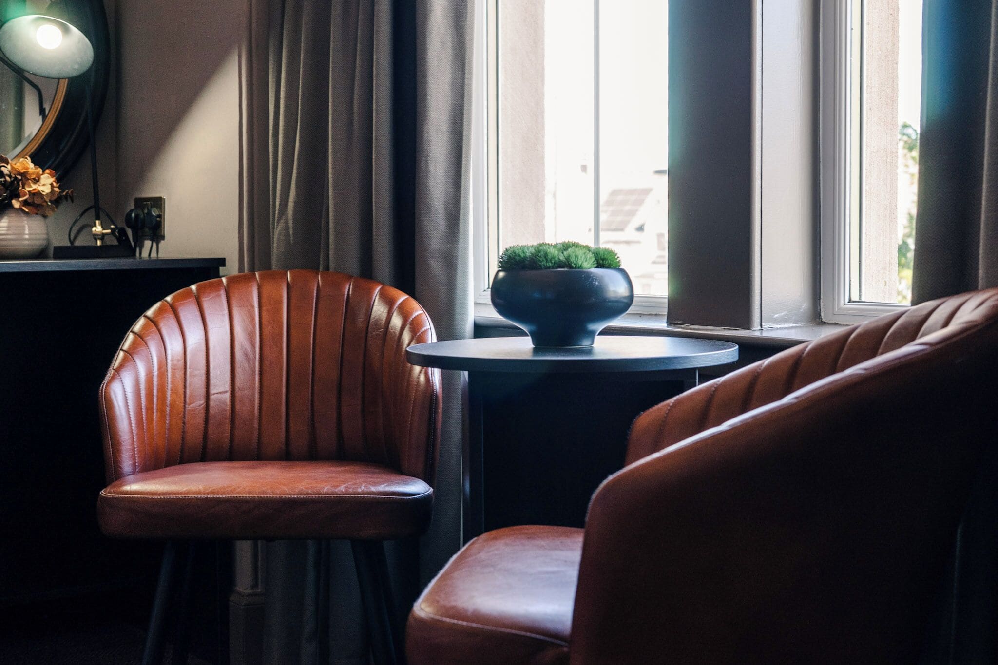 A room with a brown leather chair, a small round table with a green plant, and a window with curtains.
