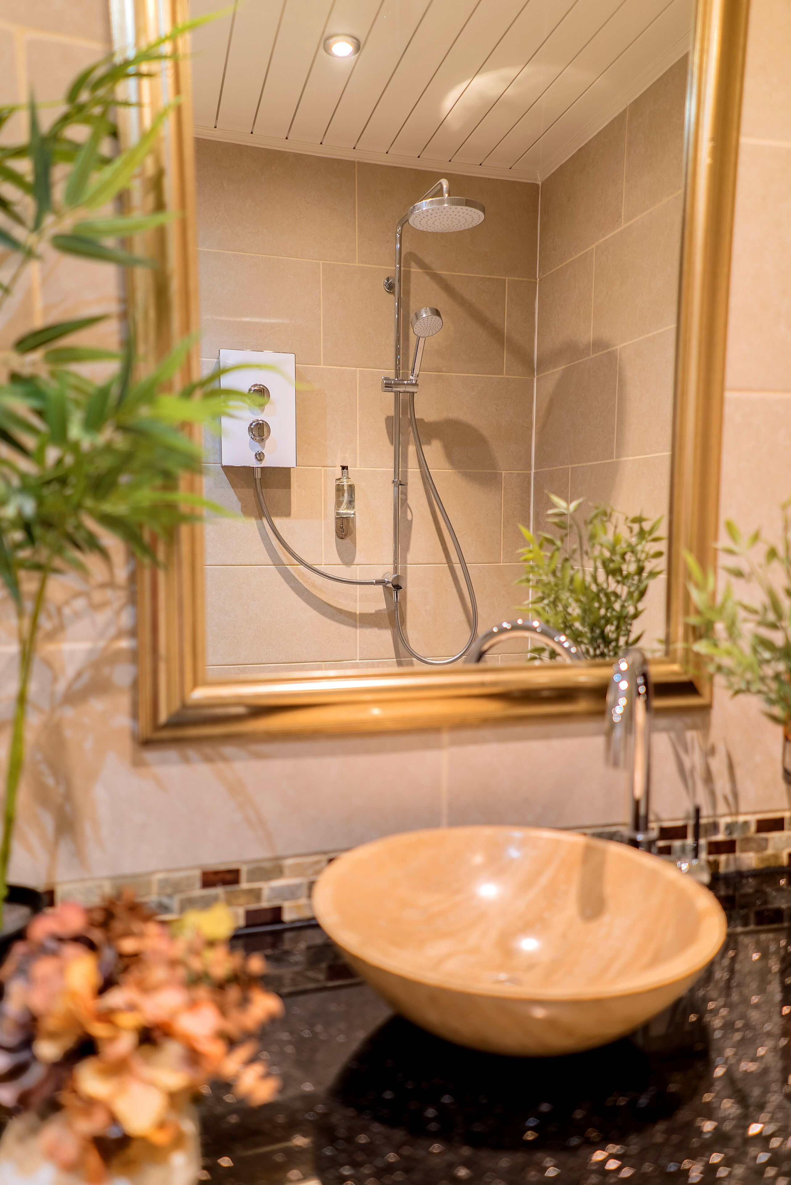 A bathroom with a beige tiled shower, a wooden sink, and a mirror with a gold frame.
