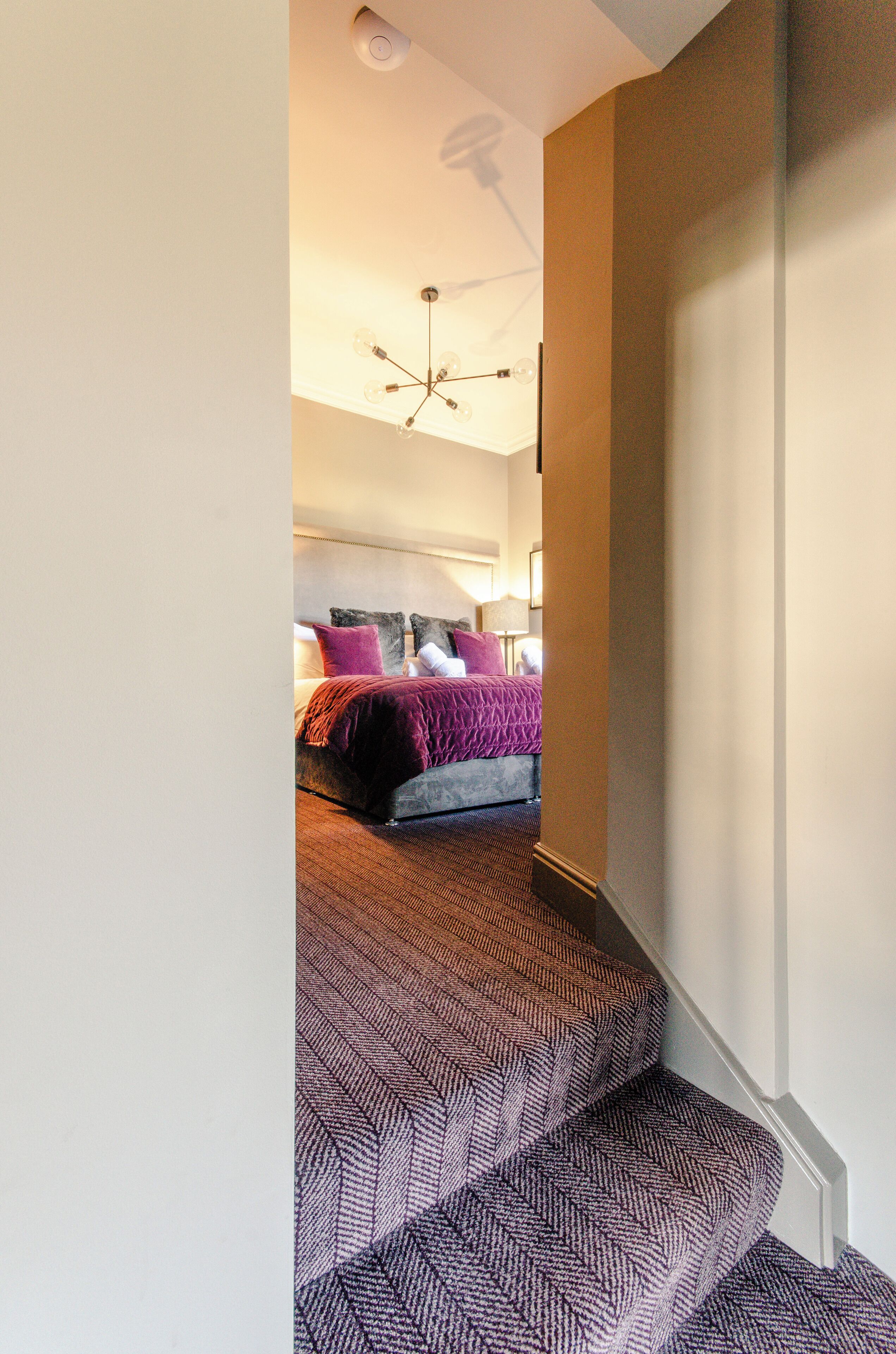 A staircase leading to a bedroom with a bed, pillows, and a ceiling light fixture.