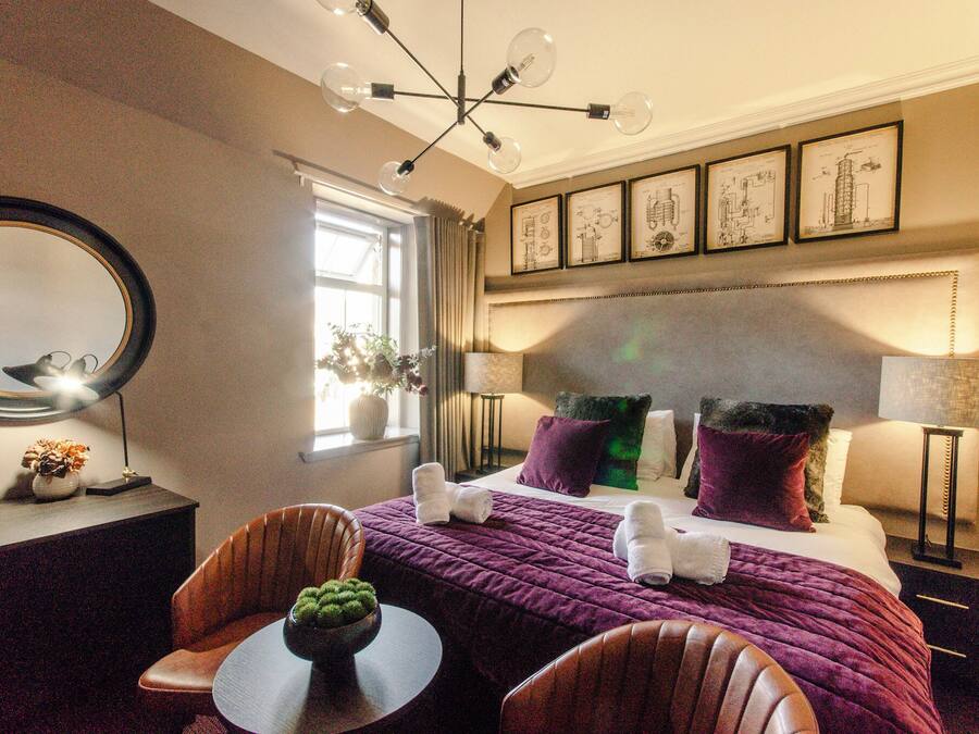 Ein Hotelzimmer mit einem großen Bett, einem runden Tisch, einem Sessel, einem Spiegel und einem Fenster mit Vorhängen.
