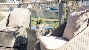 Un espace de détente extérieur aménagé avec des meubles en osier, des chaises rembourrées et une petite table agrémentée d’une plante.