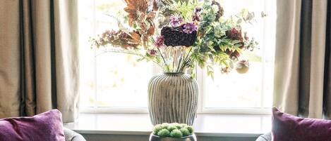 A room with two armchairs, a small table with a vase of flowers, and a window with curtains.
