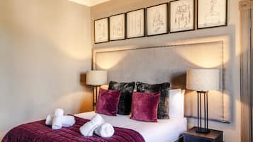 Habitación de hotel con una cama grande, dos lámparas de noche, cabecera con dibujos arquitectónicos enmarcados y mesita de noche con cajón.