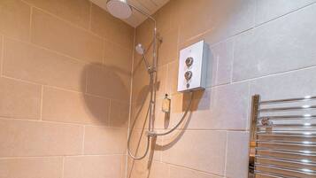 A shower area with beige tiles, a showerhead, a control panel, and a towel rack.