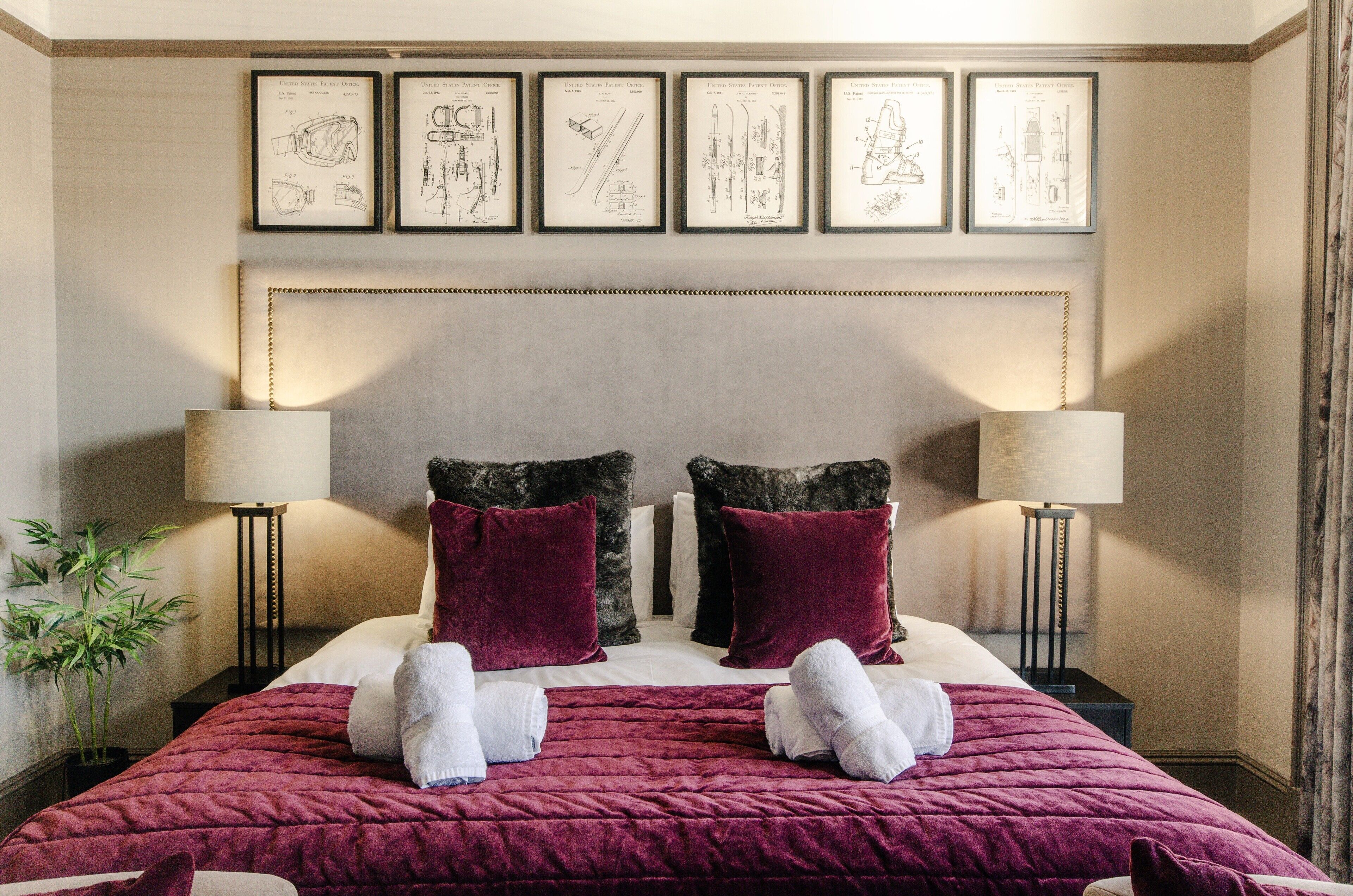 A neatly made bed with a red blanket, two pillows, and two white towels. There are framed drawings on the wall above the bed.