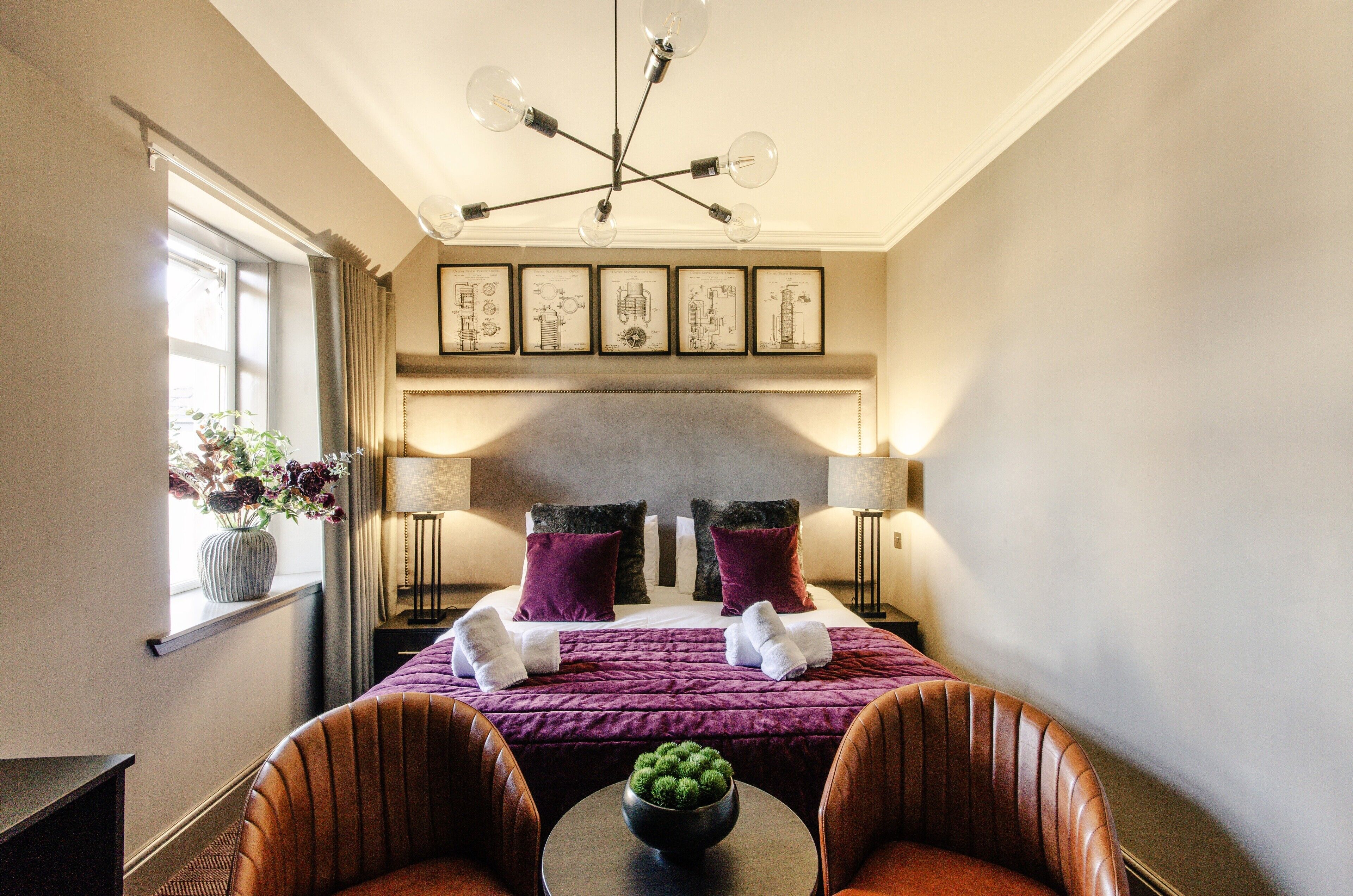 Habitación de hotel con cama, dos sillas, una mesa, un jarrón con flores y un candelabro.