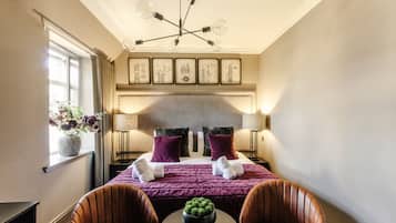 A hotel room with a bed, two chairs, a table, a vase with flowers, and a chandelier.