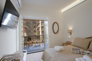 A hotel room with a bed, a chair, a table, and a balcony with a view of the city. - Suite Positano - 100 Meters From the Beach (Maiori)