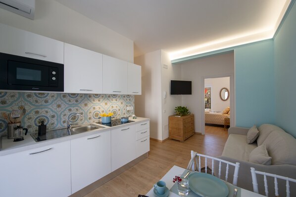 A compact kitchen with white cabinets, a black microwave, and a tiled backsplash. - Suite Positano - 100 Meters From the Beach (Maiori)