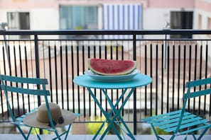 Un balcón con una mesa que sostiene una sandía, dos sillas y un sombrero en una de ellas.