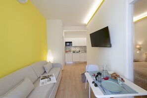A compact living space with a sofa, dining table, and a kitchen area in the background.