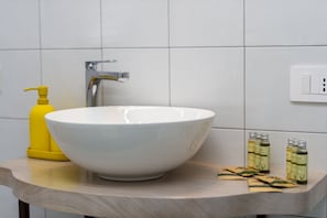 A bathroom with a white sink, a yellow soap dispenser, and several bottles of liquid soap on the countertop. - Suite Nerano - In the Center of Maiori a few Steps From the sea (Maiori)