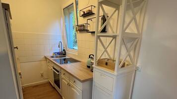 A compact kitchen with white cabinetry, a wooden countertop, a window, and a ceiling light.