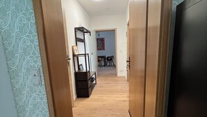 Un couloir doté d’un plancher en bois, d’un paillasson et d’une porte donnant sur une pièce où se trouvent un lit et une commode.