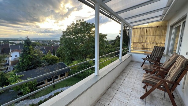 Un balcon donnant sur le paysage urbain, un espace couvert avec une table et des chaises, et une balustrade.