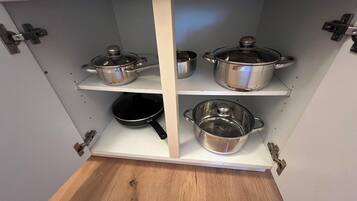 A kitchen with white cabinets and stainless steel cookware on shelves.