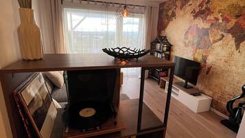 Ein Wohnzimmer mit Couchtisch aus Holz, einem Plattenspieler, einer Weltkugel an der Wand und einem Fernseher.
