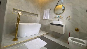 A modern bathroom with a freestanding bathtub, a vanity with a mirror, and a toilet. - PON Bliss Apartments (Abuja)