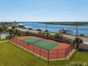 Tennisbane med udsigt over vand og en badebro.