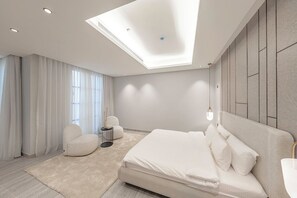 A modern bedroom with a large bed, a seating area with a chair and a small table, and a skylight above the bed.