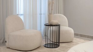 Una habitación moderna con dos sillones blancos, una mesita redonda y un florero con flores secas.