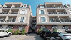 Un edificio residencial de varios pisos con entrada central, balcones y un estacionamiento con automóviles.