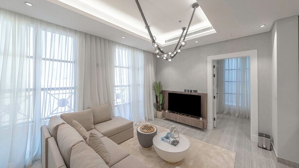 Una sala de estar moderna con un sofá seccional, un televisor de pantalla plana, una mesa de centro y una araña.
