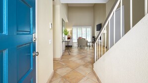 A hallway with a blue door, a staircase, and a dining area with a plant and a chair.