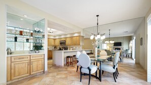A spacious kitchen with wooden cabinets, a central island, and a dining area with chairs and a chandelier.