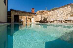 A clear swimming pool with lounge chairs and a stone wall.