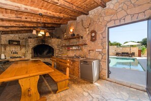 A rustic kitchen with a stone wall, wooden ceiling, and a built-in pizza oven.