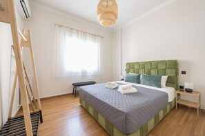 A neatly arranged bedroom with a green upholstered headboard, a bed with a grey quilt, a wooden bench, and a wicker hanging light fixture. - Stylish 2 Bd Urban Retreat Near Panormou (Athens)