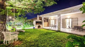 A modern house with a well-maintained lawn, outdoor seating, and a fireplace.