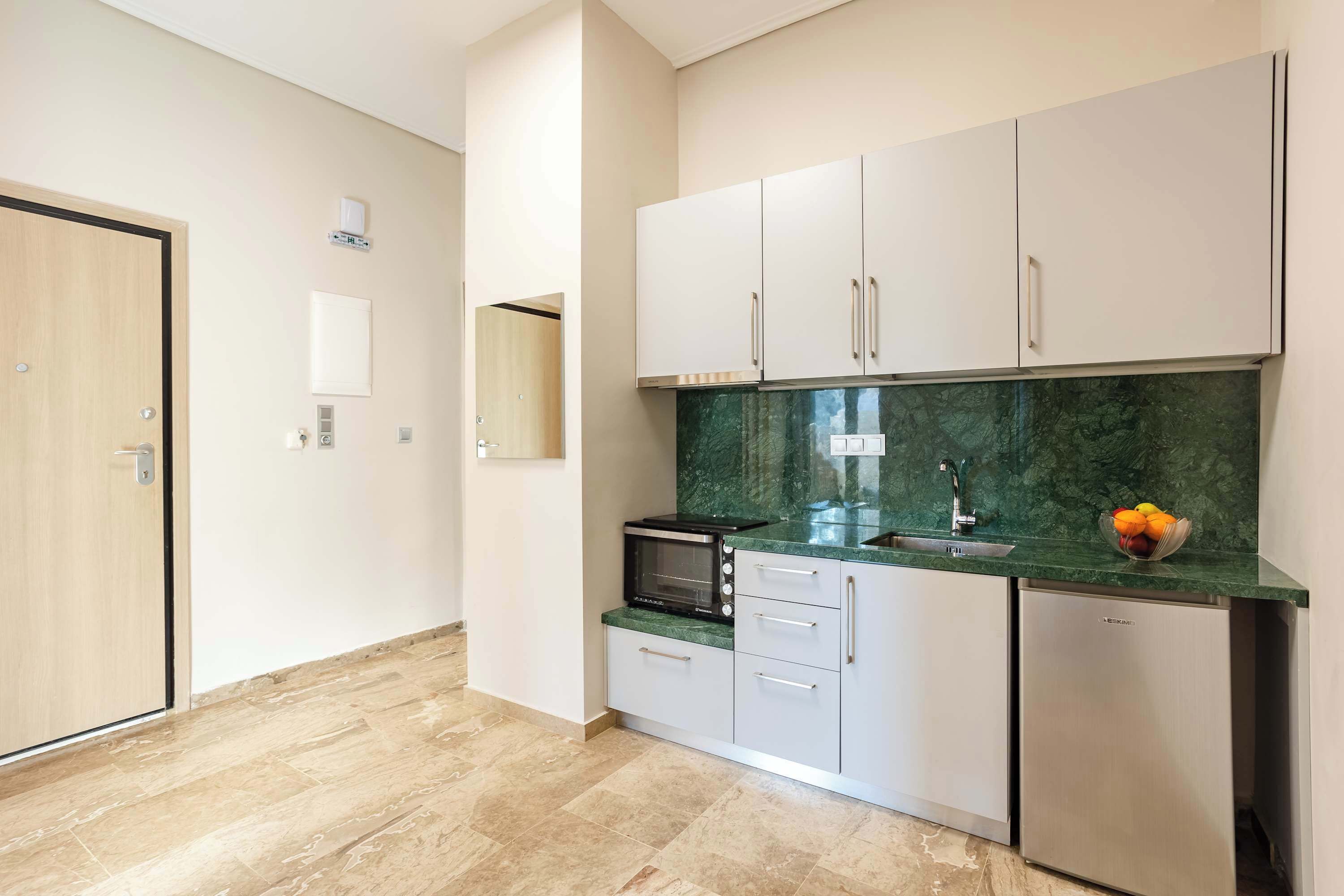 A modern kitchen with white cabinets, a microwave, a refrigerator, and a marble countertop.