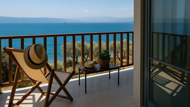 A balcony with a view of the sea, a chair, a hat, and a potted plant. - Seafront Verga Stone Haven - Waves' Embrace (Paralia Vergas)