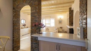 A kitchen with stone walls, a white countertop, and a view into the dining area. - Seafront Verga Stone Haven - Waves' Embrace (Paralia Vergas)