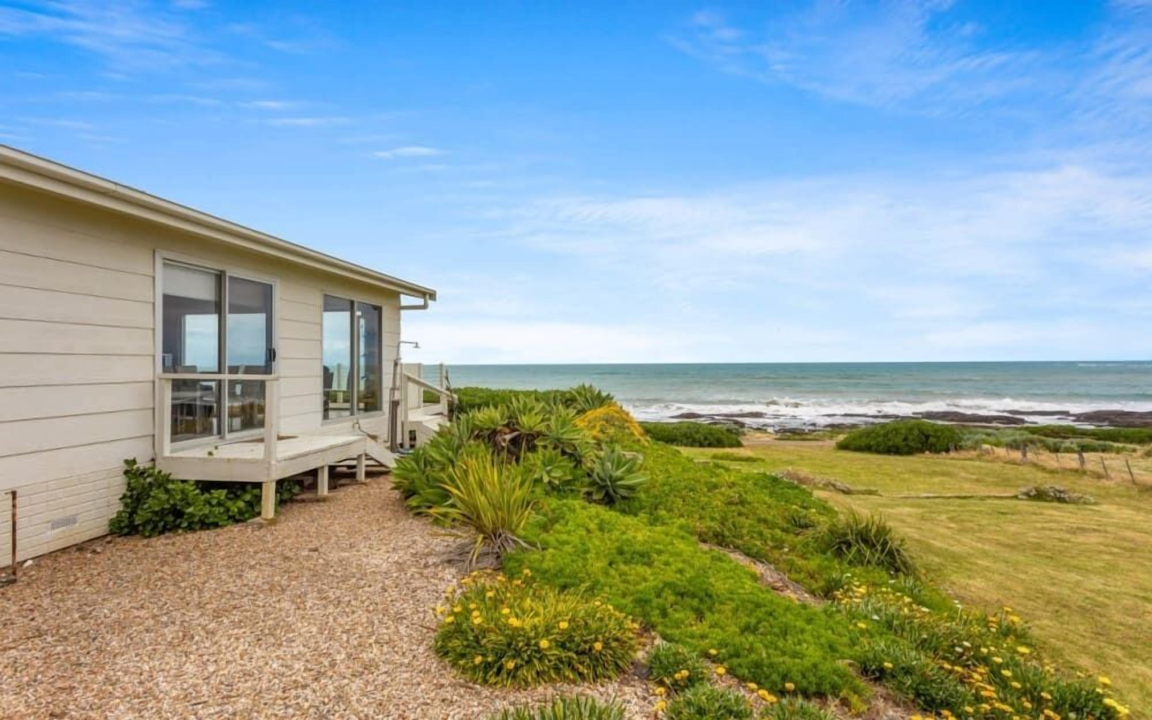 A coastal house with a deck, a gravel driveway, and a view of the ocean.