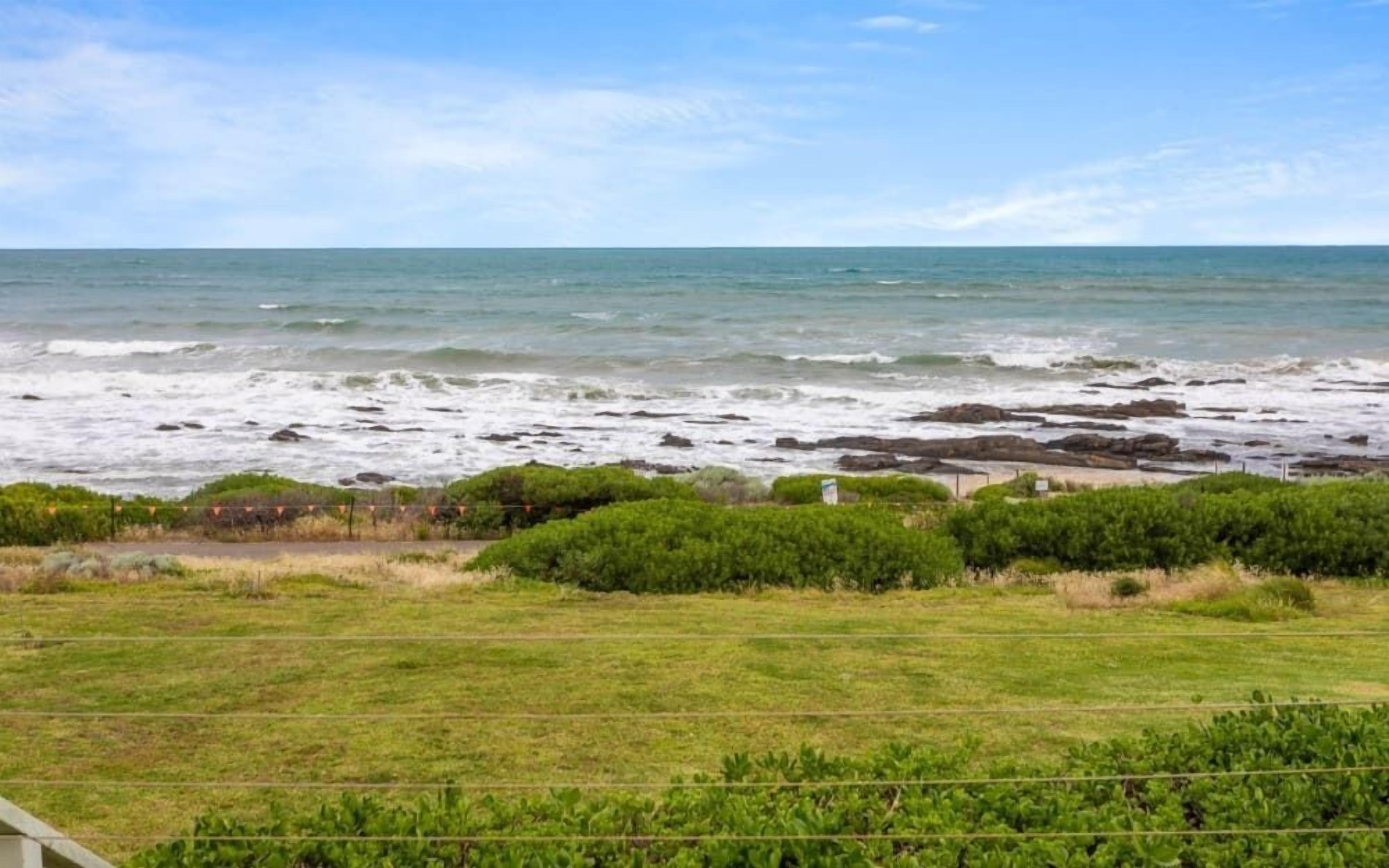 A coastal landscape with a grassy foreground, rocky shoreline, and the ocean in the background.