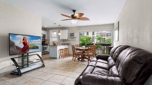 A living room with a leather sofa, a TV, a ceiling fan, and a dining area with a table and chairs.