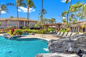 A resort pool area with clear blue water, lounge chairs, and palm trees.