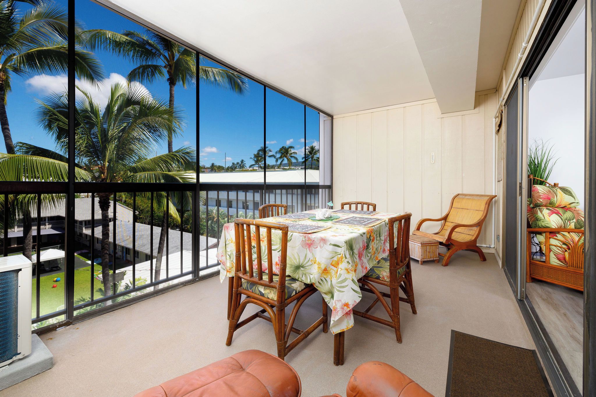 A balcony with a table and chairs, a view of palm trees, and a sliding glass door.