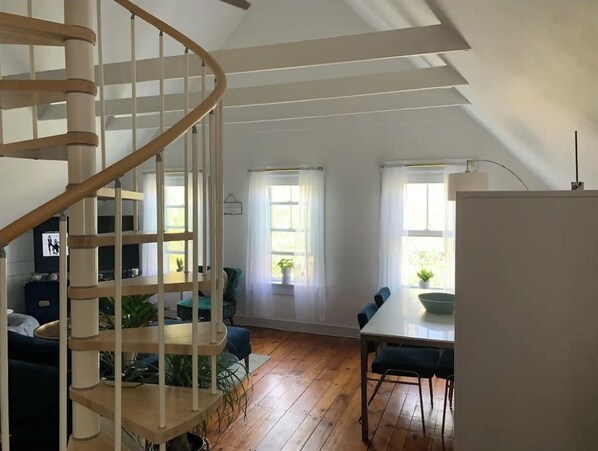 A spacious room with a spiral staircase, a dining area with a table and chairs, and large windows allowing natural light. - Serene Loft in Heart of Ptown - Steps to Commercial St, Pet Friendly (Provincetown)