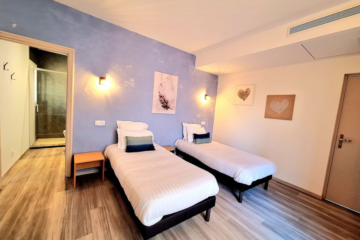 A bedroom with two beds, a shower, and a door.