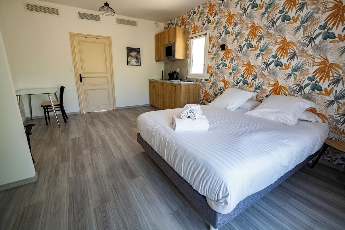 A bedroom with a large bed, a wooden nightstand, a microwave, and a window.