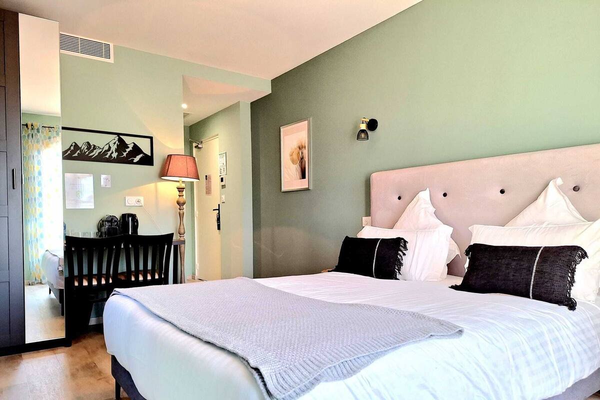 A hotel room with a large bed, a desk with a lamp, a chair, and a picture on the wall.