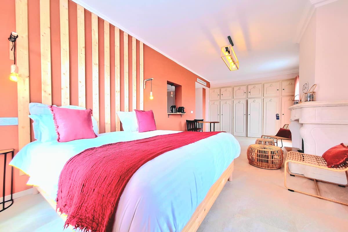 A bedroom with a large bed, wooden slats on the wall, a small table with chairs, and a fireplace.