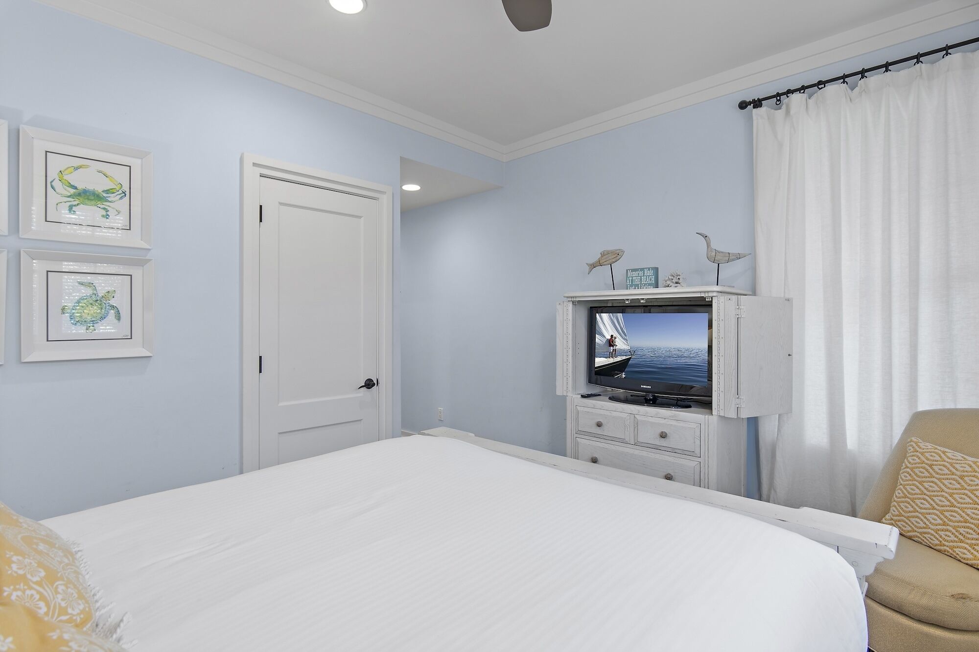 Une chambre à coucher avec un lit, un téléviseur posé sur une commode et des tableaux encadrés accrochés au mur.
