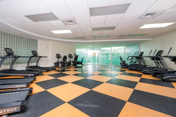 Un gimnasio con varias cintas de correr dispuestas en filas, suelo de cuadros y una pared de vidrio al fondo.