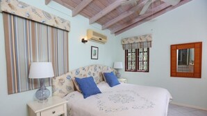 A bedroom with a bed, bedside tables, a window with curtains, a wall-mounted air conditioner, and a mirror.