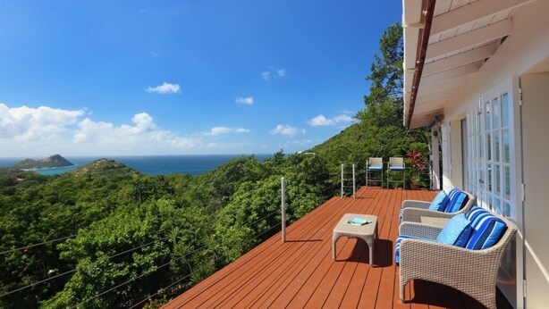 A wooden deck with wicker furniture and a view of the ocean.